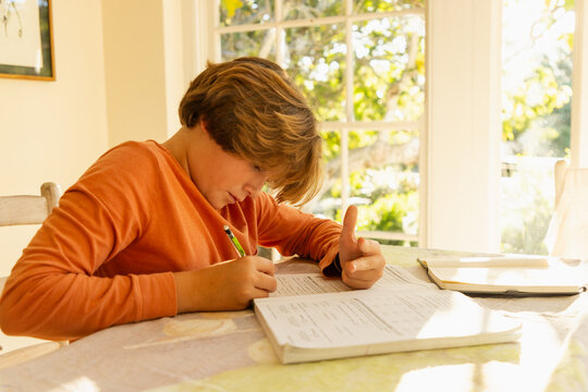 12 year old boy doing homework at kitchen table at sunset