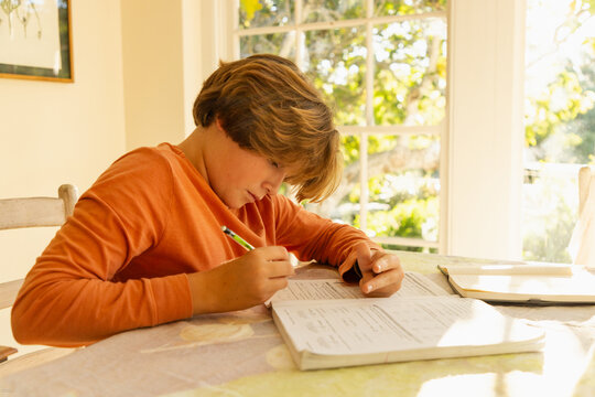 12 year old boy doing homework at kitchen table at sunset
