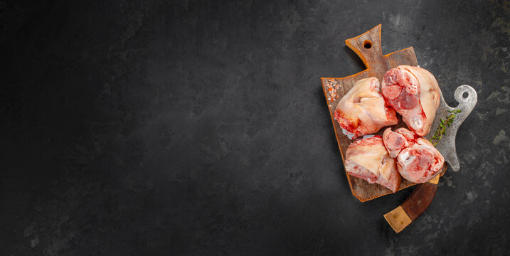 Raw meat bones on wooden board with knife over dark background copy space
