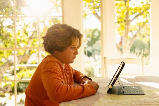 12 year old boy using tablet at home at sunset