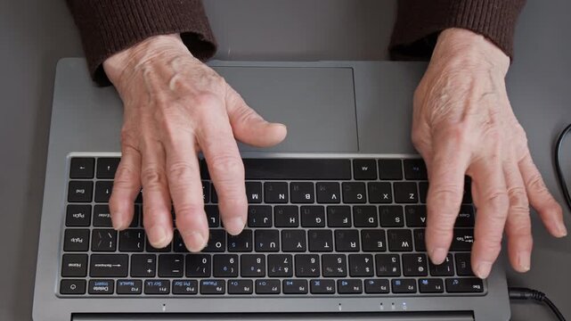 Top view close up of wrinkled hands of unrecognizable senior woman carefully typing on laptop keyboard and using internet, copy space
