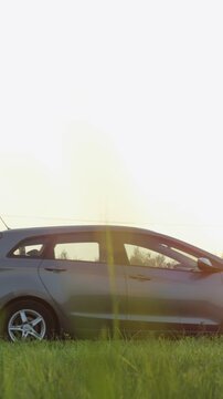 Man pushes his broken car down the road during sunset near a grassy area with trees and a clear sky in the background