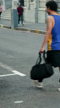 Vertical video: Entering right pedestrians walking by stone facade, man in blue tank holding duffel