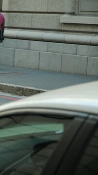 Vertical video: Walking blond lady in blue suit moving left on city curb, passing phone, copy space