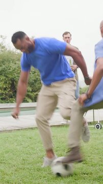 Vertical video: Ball rolling striped tee man dribbling for control on lawn joining friends by grill