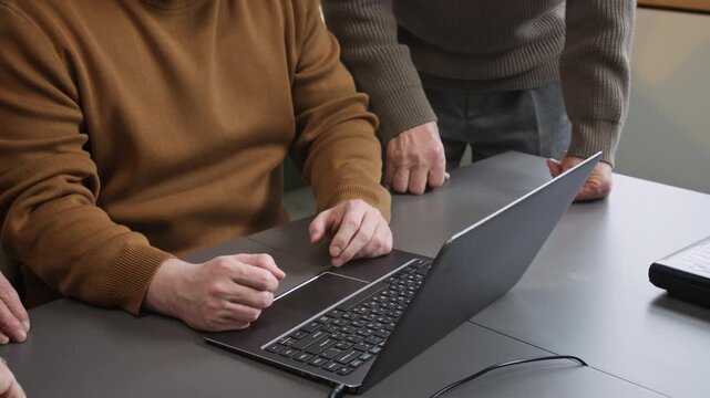 Close up shot of open laptop on desk in classroom with hands pointing while unrecognizable male teacher leading class for seniors, copy space
