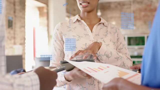 Woman leading data review after peer pointing device at tablet tapping showing blue chart overlays
