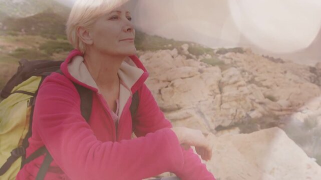Senior female hiker pausing on cliff for wellness, gazing horizon while bokeh drifting over face