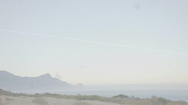 Coast ridge and horizon silhouetting as plume rising from shore causing haze, showing light shifts