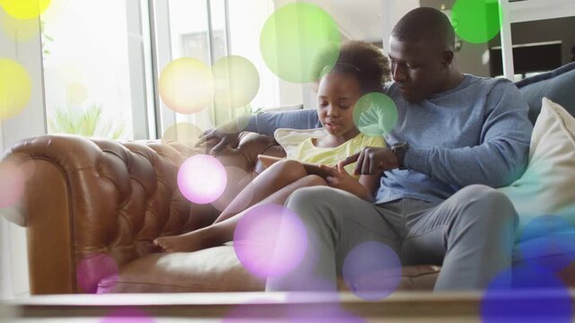 Man leaning in guiding girl tapping tablet on sofa, starting learning lesson with drifting overlays