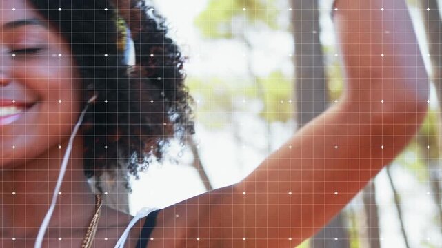 Woman inserting earphones, switching to over-ear under sunlit trees, grid-sparkle syncing for music