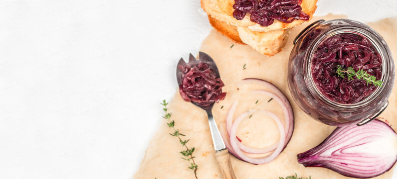 Onion jam in glass jar with bread and ingredients on light background with copy space top view