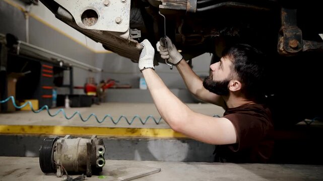 Mechanic diagnosing car undercarriage, performing vehicle inspection and repair in an auto service garage