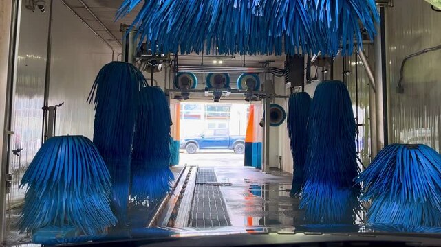 Automated drive-through car wash tunnel with blue brushes.