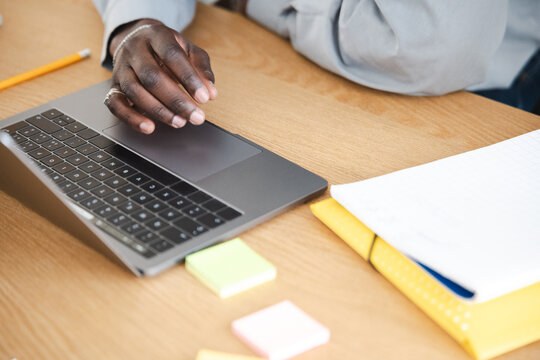 A person's hands are on a laptop keyboard, with sticky notes and notebooks on a wooden desk, suggesting work or study.