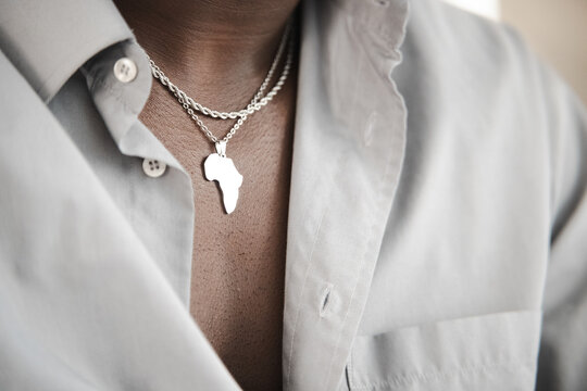 A person wears a silver necklace with a pendant shaped like the continent of Africa over a light-colored button-down shirt.