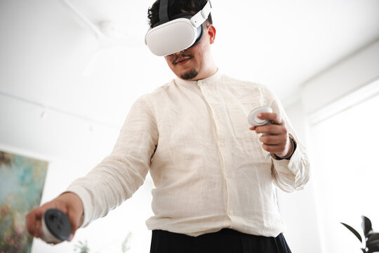 A man wearing a virtual reality headset and holding controllers engages with an immersive digital experience, exploring new dimensions.