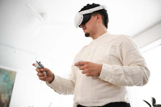 A man wearing a virtual reality headset and holding controllers engages with an immersive digital experience, exploring new worlds and interacting with virtual environments.