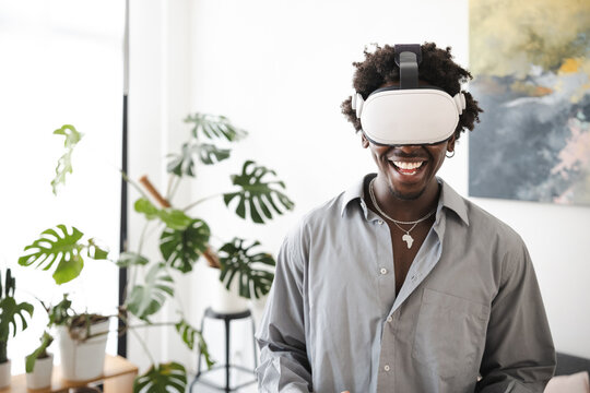 A smiling man wearing a virtual reality headset experiences immersive technology in a modern living room with plants.