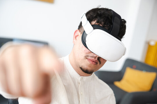 A young man wearing a virtual reality headset reaches out his hand while immersed in a digital world.