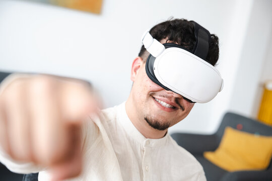 A man wearing a virtual reality headset smiles as he reaches out his hand, engaging with an immersive digital experience.