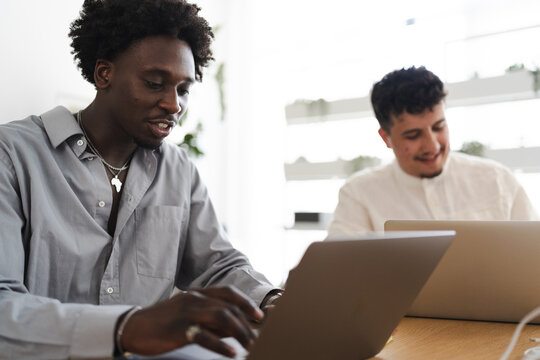 Two men collaborate on laptops in a bright, modern office space, focusing on their work and shared project.