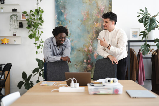 Two men in a modern office space are engaged in a lively conversation, one gesturing while the other smiles, suggesting collaboration and idea sharing.
