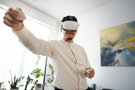 A man wearing a virtual reality headset and holding controllers engages with an immersive digital experience in a bright, modern room.