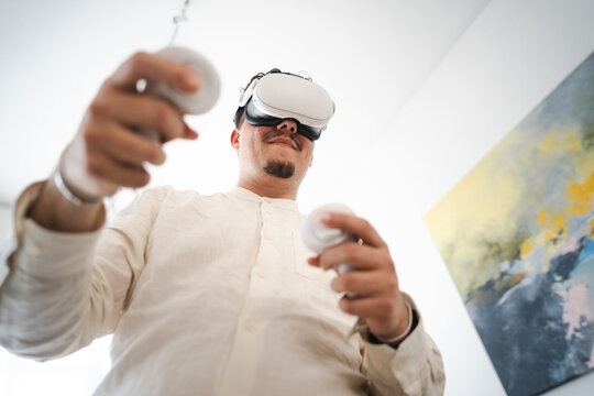 A man wearing a virtual reality headset and holding controllers engages with immersive digital content, exploring new dimensions of entertainment and interaction.