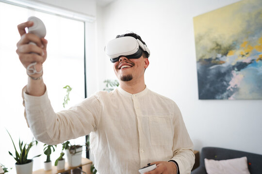 A man wearing a virtual reality headset and holding controllers engages with an immersive digital experience in a bright, modern room.