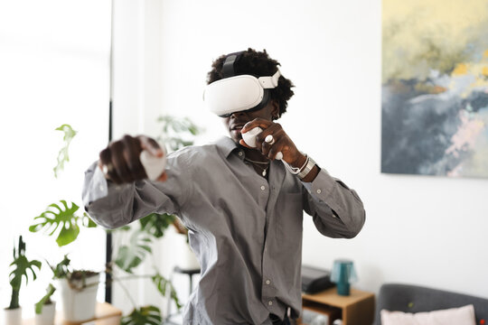 A young man wearing a virtual reality headset and holding controllers engages in an immersive digital experience at home.