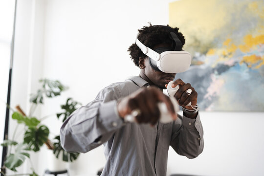 A young man wearing a virtual reality headset and holding controllers engages in an immersive digital experience, his hands extended forward.