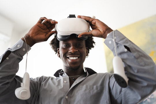 A smiling man adjusts a virtual reality headset, holding controllers, ready to enter an immersive digital world.