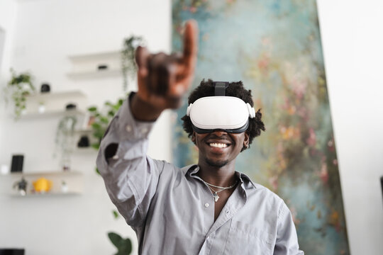 A smiling man wearing a virtual reality headset points his finger forward, engaging with an immersive digital experience in a modern room.