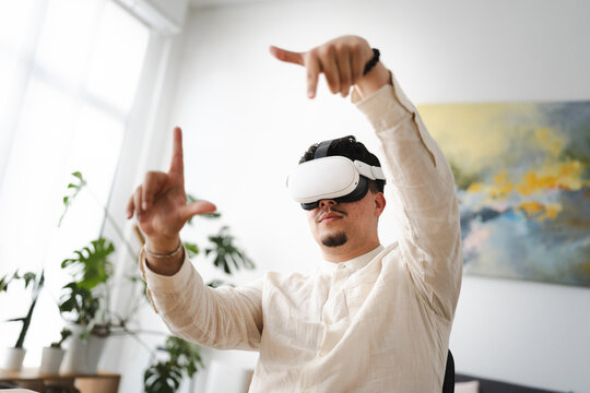 A man wearing a virtual reality headset interacts with a digital interface, his hands gesturing to manipulate virtual objects in an immersive experience.