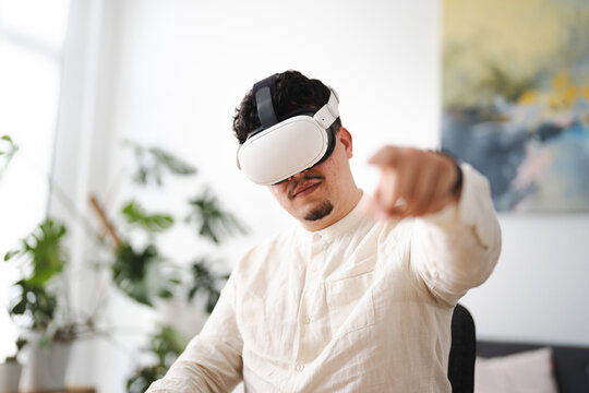 A man wearing a virtual reality headset points forward, engaging with an immersive digital experience in a modern, plant-filled room.