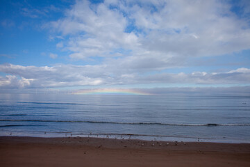 Obraz premium horizontal arc rainbow, an optical phenomenon formed by refraction of sunlight in ice crystals suspended in atmosphere, on horizon of North Sea at Aberdeen beach with gulls and offshore wind turbines 