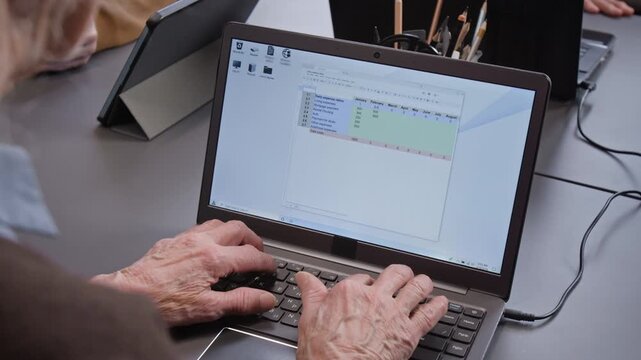 Over shoulder shot of unrecognizable senior woman typing on keyboard and filling in data learning to use software with spreadsheets on laptop screen during computer class for seniors, copy space