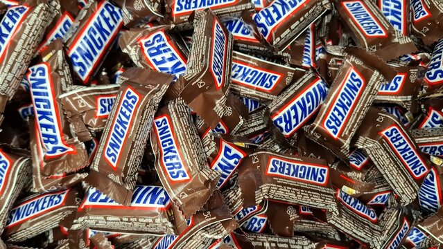 Close-up of numerous Snickers Fun Size bars scattered together. Vibrant display of popular branded confectionery. Chocolate bars with nuts and caramel. Russia, Moscow, April 29, 2026