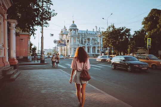 Young woman with bag walking city street with beautiful architecture on sunny summer day
