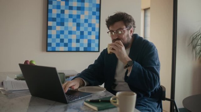 Mature adult Caucasian male writer sitting at kitchen counter, eating sandwich and finishing work on his novel, getting satisfied with result