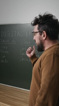 Vertical side view shot of friendly male teacher speaking in computer literacy class and pointing at board with shortcut combinations, story format
