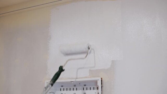 Person painting wall with brush roller near electrical box. Interior renovation and home improvement process