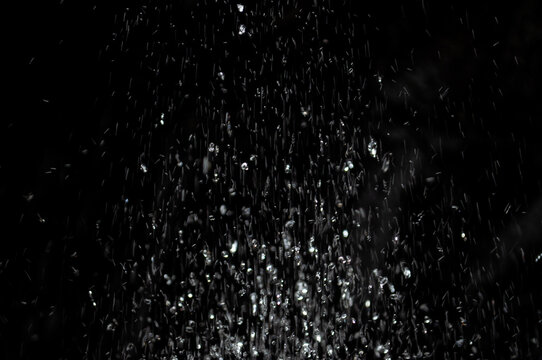Water droplets fall from a height creating a curtain of water in a dark space at night