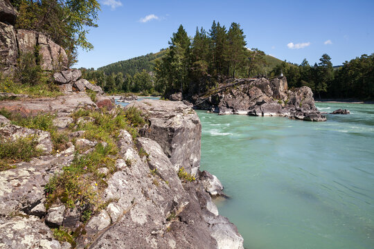 A turquoise mountain river winds around rugged rock cliffs and forested banks under a clear blue sky, evoking peaceful, adventurous outdoor feelings and pristine natural landscape scenery. Katun river