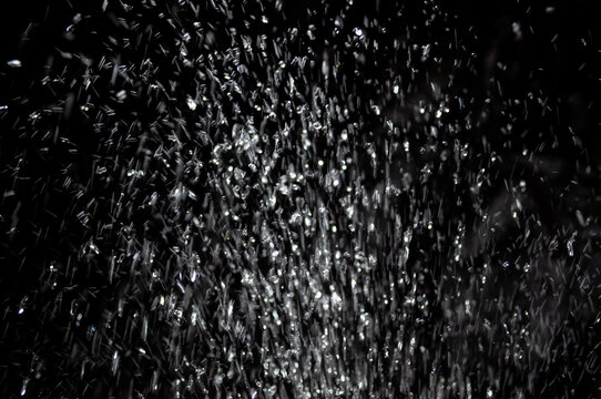 Water droplets fall from a height creating a curtain of water in a dark space at night