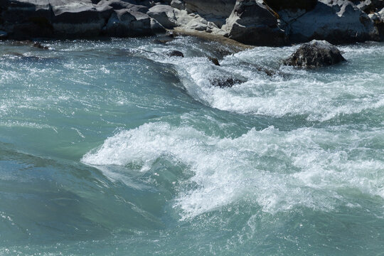 Turquoise mountain river rapids cascade over a rocky riverbed, creating foamy white water and strong currents; an outdoor nature scene conveying movement, freshness, power and adventurous spirit