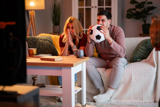 Couple watching football match, expressing stress and excitement