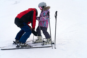 Obraz premium A children's mountain instructor adjusts the buckles on a boot to the size of a child's foot before training on the ski slope.
