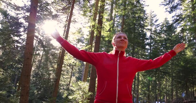 Young woman enjoys at beautiful sunset in pine forest mountain, slow motion, closeup of happy woman spreads her arms and bright sun, branches of the pine trees, season travel nature idyllic